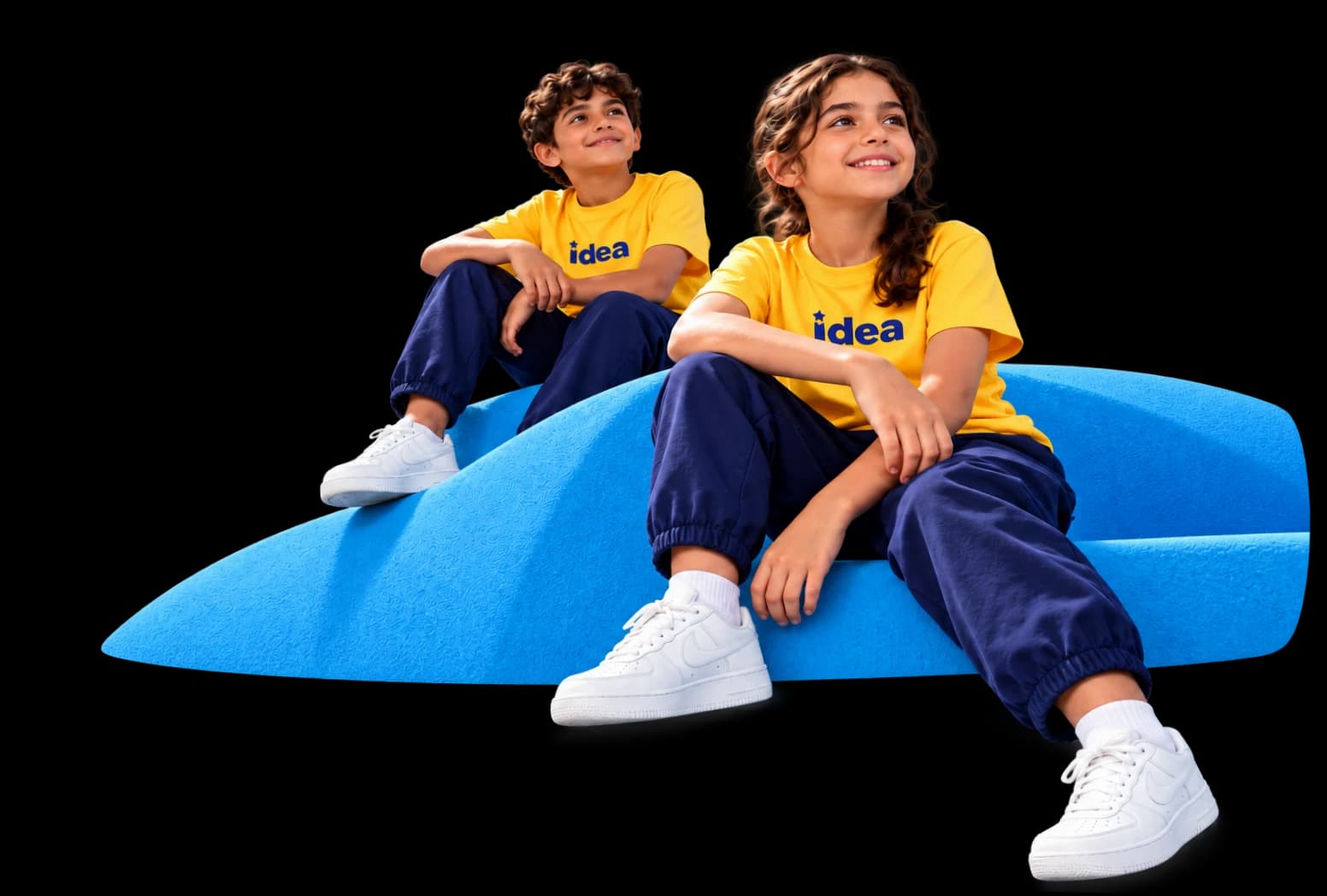 Two smiling children in yellow IDEA T-shirts sitting on a blue hill